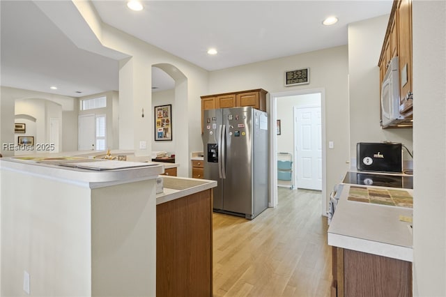 kitchen with stove, light hardwood / wood-style flooring, kitchen peninsula, and stainless steel fridge with ice dispenser