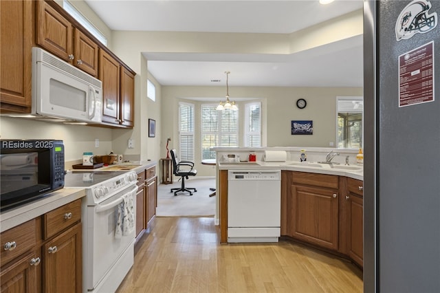 kitchen featuring sink, a notable chandelier, pendant lighting, white appliances, and light hardwood / wood-style floors