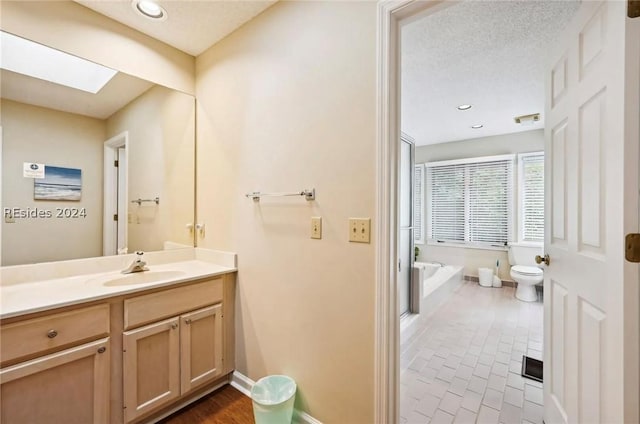 bathroom with toilet, a skylight, a textured ceiling, vanity, and a bathtub