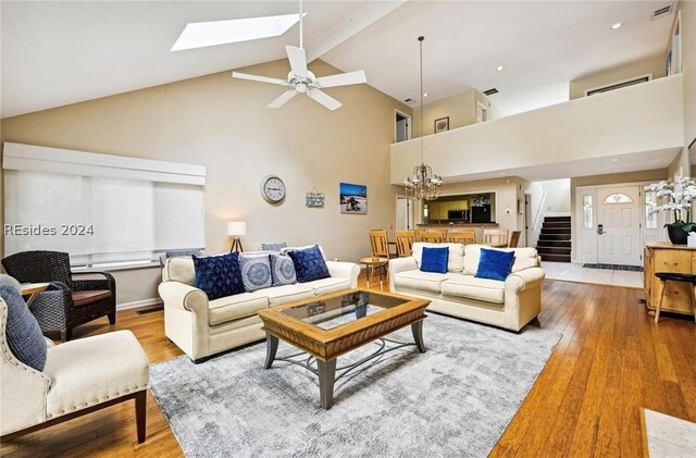 living room featuring ceiling fan with notable chandelier, high vaulted ceiling, a skylight, beamed ceiling, and wood-type flooring