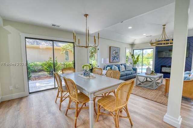 dining space with an inviting chandelier, a fireplace, and light hardwood / wood-style flooring