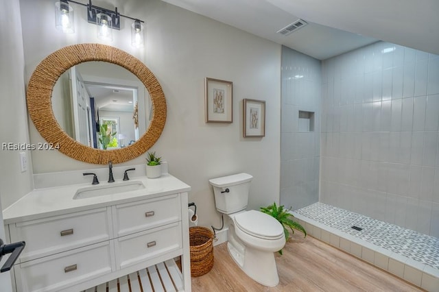 bathroom featuring hardwood / wood-style floors, vanity, a tile shower, and toilet