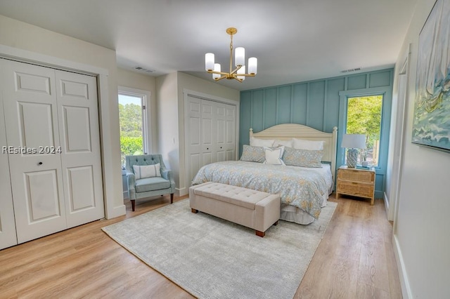 bedroom featuring a notable chandelier, light hardwood / wood-style floors, and multiple closets