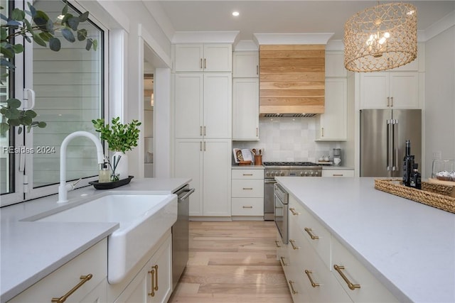 kitchen with tasteful backsplash, white cabinetry, decorative light fixtures, premium appliances, and light hardwood / wood-style floors