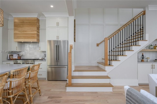 kitchen with tasteful backsplash, white cabinetry, high end fridge, and light hardwood / wood-style flooring