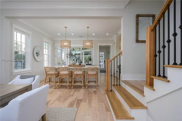 kitchen with ornamental molding, decorative light fixtures, a breakfast bar, and light hardwood / wood-style flooring