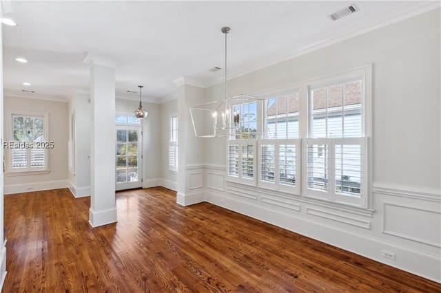 unfurnished dining area featuring ornate columns, crown molding, dark hardwood / wood-style floors, and an inviting chandelier