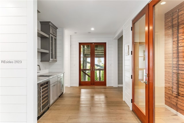 kitchen with gray cabinets, light hardwood / wood-style flooring, wine cooler, light stone countertops, and french doors