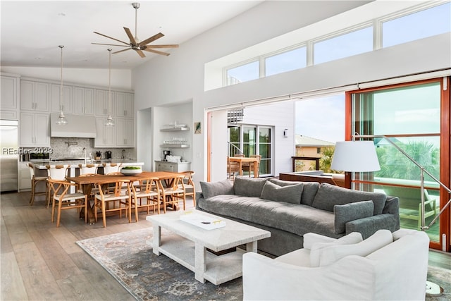 living room featuring light hardwood / wood-style flooring, high vaulted ceiling, and ceiling fan