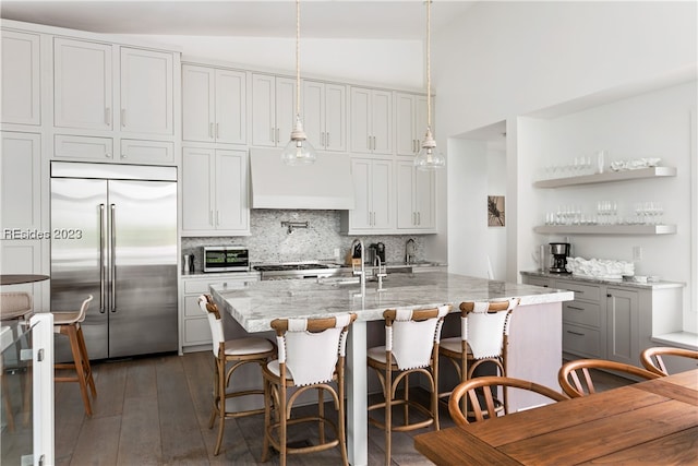 kitchen featuring light stone counters, built in refrigerator, vaulted ceiling, custom range hood, and pendant lighting