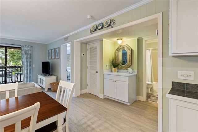 dining room featuring crown molding, sink, a textured ceiling, and light hardwood / wood-style flooring