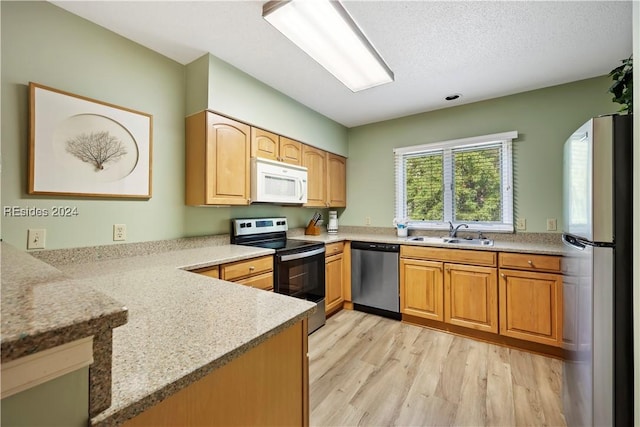 kitchen with sink, stainless steel appliances, kitchen peninsula, and light wood-type flooring