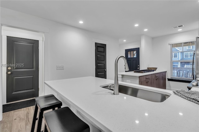 kitchen with sink, stainless steel fridge, a kitchen bar, dark brown cabinets, and light wood-type flooring