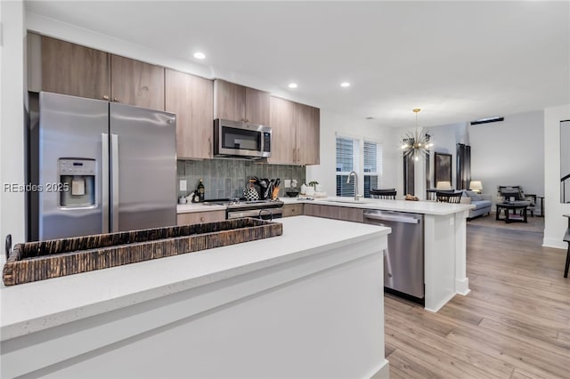 kitchen featuring decorative light fixtures, sink, decorative backsplash, light hardwood / wood-style floors, and stainless steel appliances