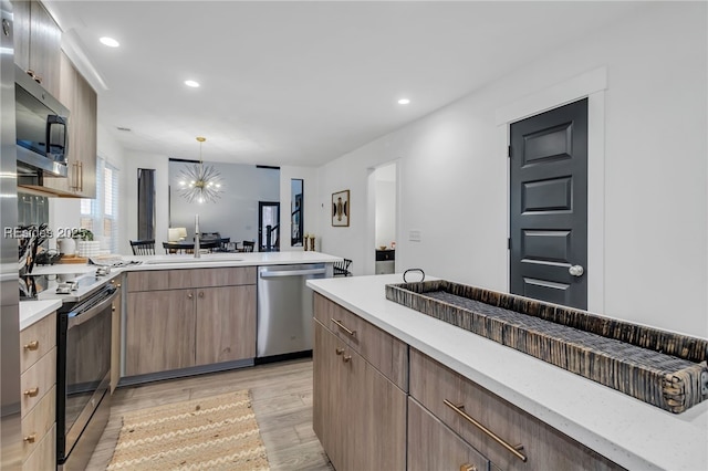 kitchen featuring appliances with stainless steel finishes, pendant lighting, sink, light wood-type flooring, and an inviting chandelier