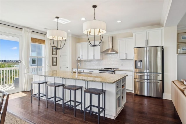 kitchen with stainless steel appliances, a kitchen island with sink, wall chimney range hood, and white cabinets