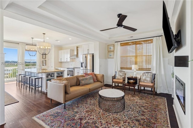 living room featuring ceiling fan with notable chandelier, a tray ceiling, dark hardwood / wood-style flooring, and sink