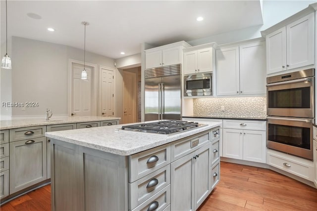 kitchen featuring sink, tasteful backsplash, built in appliances, light wood-type flooring, and pendant lighting