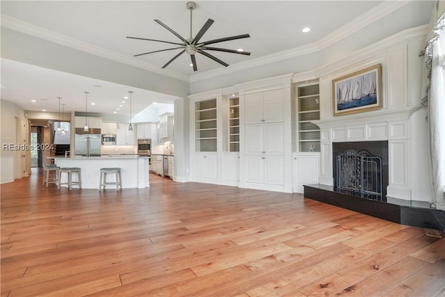 unfurnished living room featuring built in features, ornamental molding, ceiling fan, and light wood-type flooring