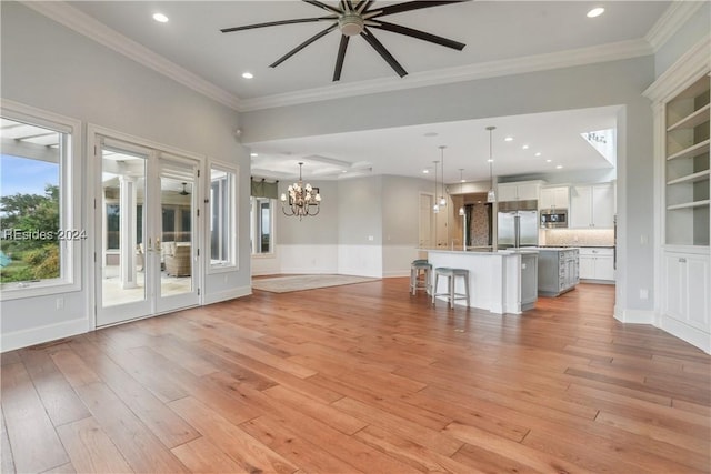 unfurnished living room with ornamental molding, ceiling fan with notable chandelier, and light wood-type flooring