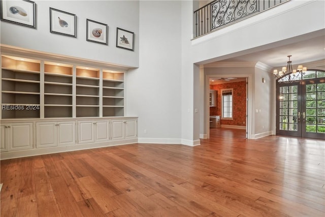 unfurnished living room with a towering ceiling, built in features, french doors, and a chandelier