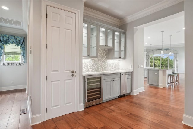 bar with crown molding, tasteful backsplash, hanging light fixtures, light hardwood / wood-style flooring, and beverage cooler