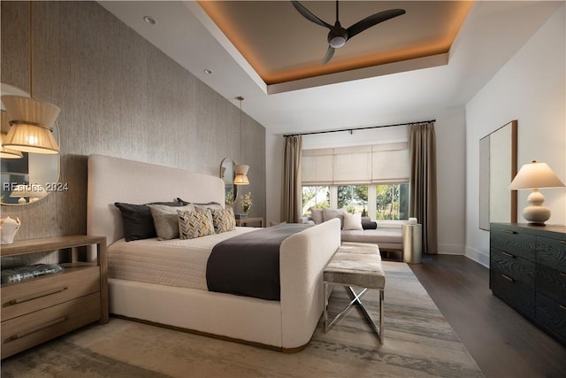 bedroom with dark hardwood / wood-style floors, ceiling fan, and a tray ceiling