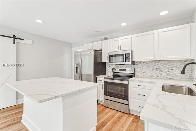 kitchen featuring sink, a center island, appliances with stainless steel finishes, a barn door, and white cabinets