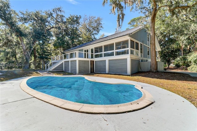 rear view of property featuring a sunroom and a covered pool