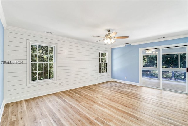 empty room featuring crown molding, wood walls, ceiling fan, and light wood-type flooring