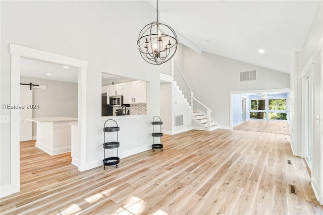 living room with an inviting chandelier, light hardwood / wood-style flooring, high vaulted ceiling, and a barn door