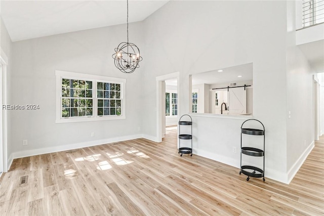 unfurnished living room with light hardwood / wood-style floors, a barn door, a chandelier, and a high ceiling