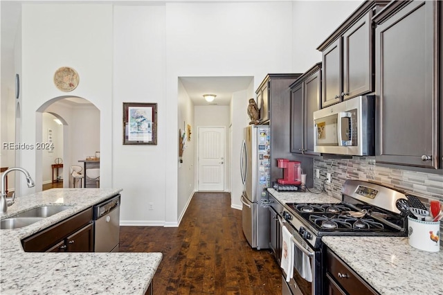 kitchen with sink, backsplash, dark brown cabinets, stainless steel appliances, and light stone counters