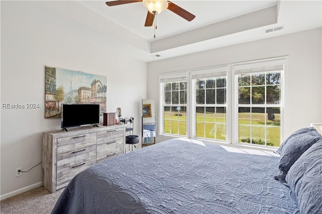 bedroom featuring light carpet, a tray ceiling, and ceiling fan