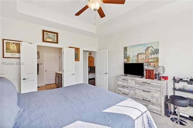 bedroom featuring ceiling fan, a tray ceiling, and ensuite bath