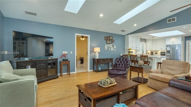 living room featuring ceiling fan, vaulted ceiling with skylight, and light hardwood / wood-style floors