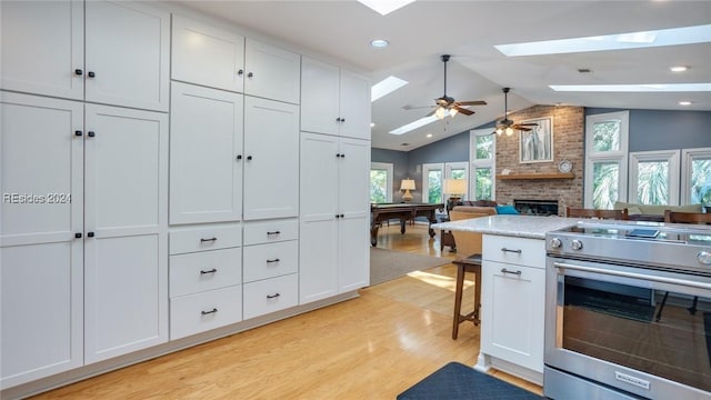 kitchen with a fireplace, stainless steel electric stove, lofted ceiling with skylight, and white cabinets