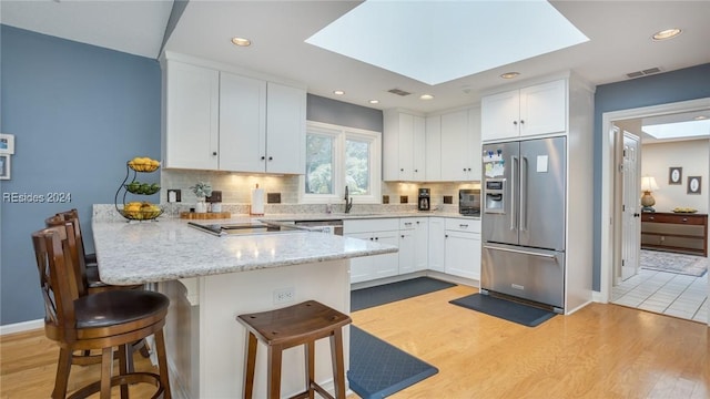 kitchen featuring high end fridge, a skylight, kitchen peninsula, and white cabinets