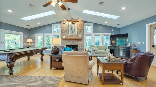 living room with a brick fireplace, vaulted ceiling with skylight, and light wood-type flooring