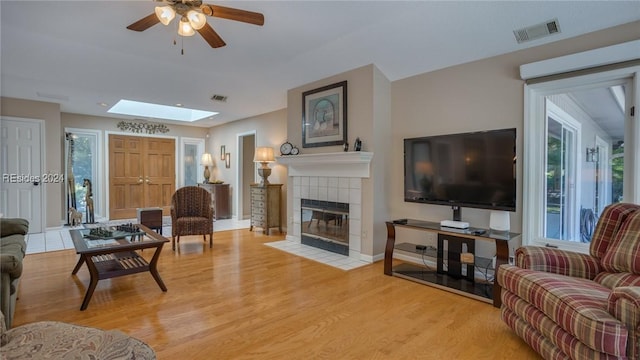 living room featuring wood-type flooring, a healthy amount of sunlight, a fireplace, and a skylight