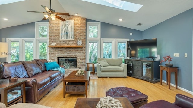 living room with vaulted ceiling, a brick fireplace, ceiling fan, and light wood-type flooring