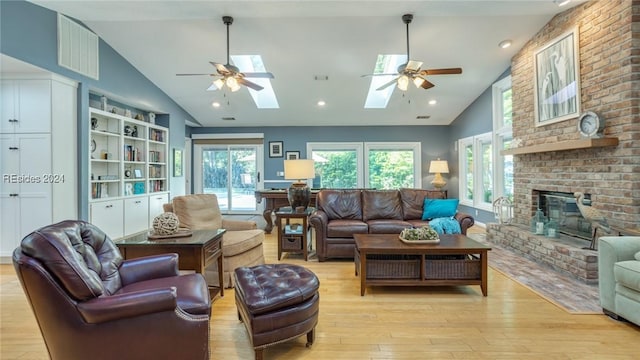 living room featuring ceiling fan, a fireplace, lofted ceiling with skylight, and light wood-type flooring