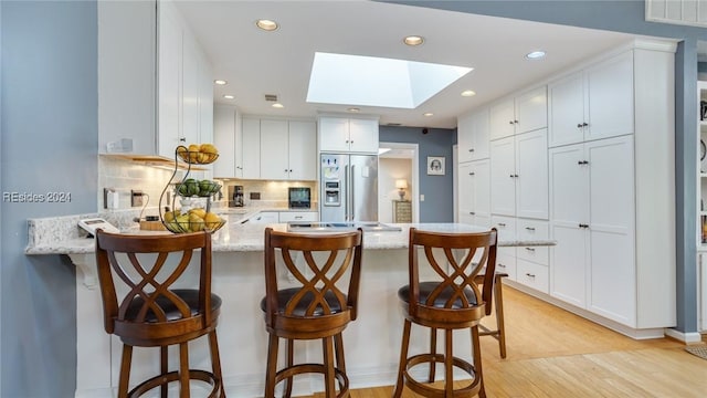 kitchen with a breakfast bar, a skylight, white cabinetry, kitchen peninsula, and stainless steel refrigerator with ice dispenser