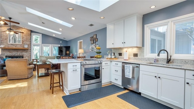 kitchen featuring sink, appliances with stainless steel finishes, white cabinets, a kitchen bar, and kitchen peninsula