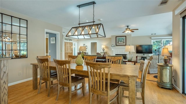 dining area with a tile fireplace, ceiling fan, and light wood-type flooring