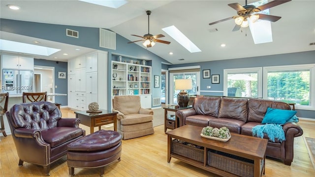 living room with ceiling fan, light hardwood / wood-style flooring, and vaulted ceiling with skylight