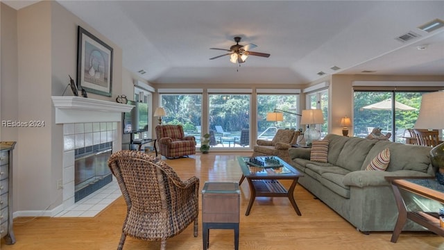 living room with a healthy amount of sunlight, vaulted ceiling, a tile fireplace, and light wood-type flooring