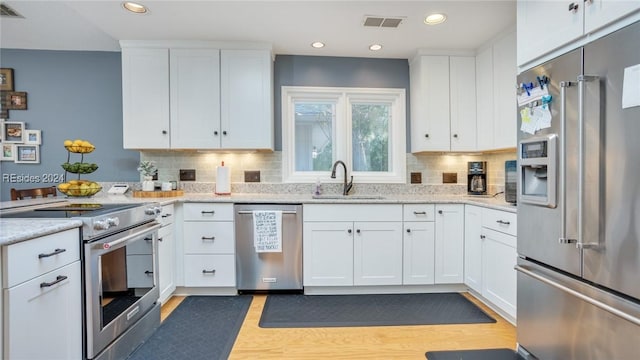 kitchen with tasteful backsplash, white cabinetry, sink, premium appliances, and light stone countertops