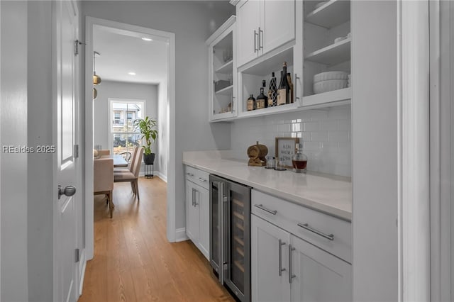 bar featuring tasteful backsplash, light hardwood / wood-style flooring, beverage cooler, and white cabinets