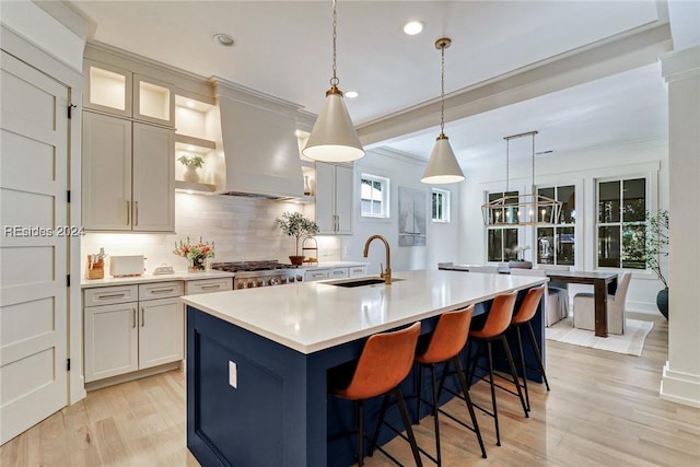 kitchen with sink, backsplash, hanging light fixtures, an island with sink, and island exhaust hood